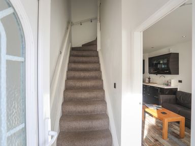 A carpeted staircase leading upstairs with a view into a kitchen and living area with a sofa and wooden coffee table at The Old Post Office 23 High Street in Cemaes Bay