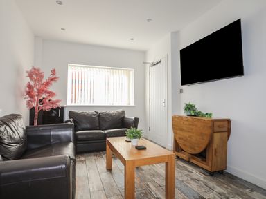 A living room with two black leather sofas a wooden coffee table a wall-mounted tv and a wooden cabinet with plants at The Old Post Office 23 High Street in Cemaes Bay