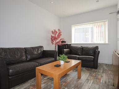 A living room with two black leather sofas a wooden coffee table with a plant and coasters and a window with vertical blinds at The Old Post Office 23 High Street in Cemaes Bay
