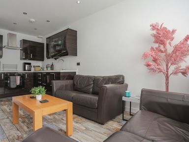 A living area with brown leather sofas a wooden coffee table with a plant and a kitchen with dark cabinets at The Old Post Office 23 High Street in Cemaes Bay