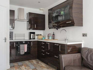 A kitchen with dark wood cabinets white countertops a sink an oven a coffee machine and a leather chair at The Old Post Office 23 High Street in Cemaes Bay