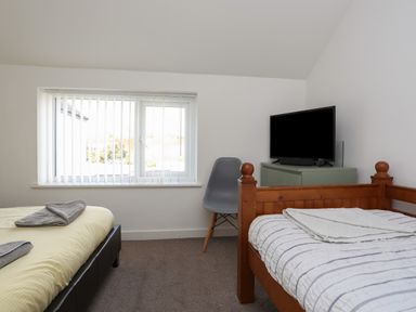 A bedroom with two beds a grey chair a small green cabinet and a television near a window at The Old Post Office 23 High Street Cemaes Bay