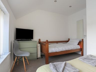 A bedroom with a wooden bed, green chest of drawers with a television, a gray chair and a bed with towels at The Old Post Office 23 High Street in Cemaes Bay