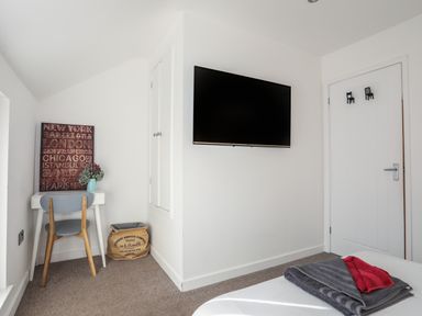 A bedroom corner with a wall-mounted TV desk and chair next to a laundry bag and a door with hooks at The Old Post Office 23 High Street in Cemaes Bay