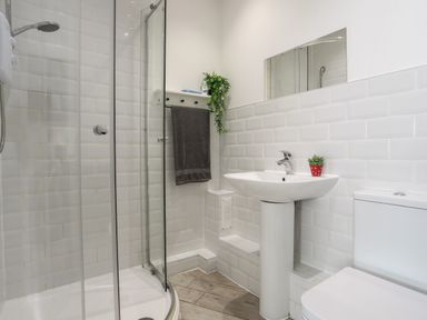 A bathroom with a glass shower enclosure a pedestal sink with a small plant a toilet and a gray towel hanging on a rack at The Old Post Office 23 High Street in Cemaes Bay