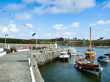 A harbor with boats docked near a stone pier with benches and flags at The Old Post Office 23 High Street in Cemaes Bay