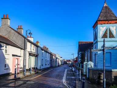 A street with white houses on one side and a blue building with signs on the other at The Old Post Office 23 High Street in Cemaes Bay