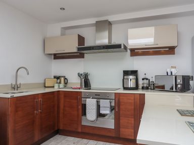 A kitchen with wooden lower cabinets beige upper cabinets a stainless steel oven stove and hood a toaster kettle coffee machine microwave and a sink at The Studio @ The Old Post Office in Cemaes Bay