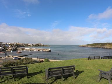 A grassy area with benches overlooking a harbor with boats and houses at The Studio @ The Old Post Office in Cemaes Bay