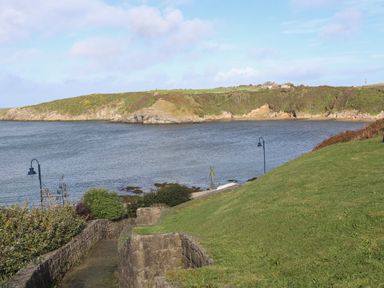 A coastal view with grassy slopes stone walls and water at The Studio @ The Old Post Office in Cemaes Bay