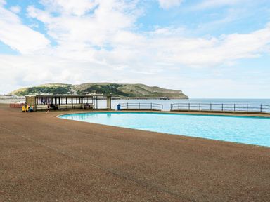 An outdoor swimming pool by the sea with a shelter and distant hills at Little Orme View in Llandudno