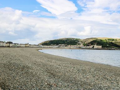 A rocky beach beside a body of water with buildings and hills in the background at Little Orme View in Llandudno