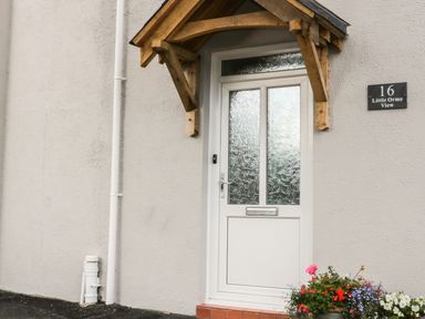 A white front door with textured glass panels under a wooden canopy with flowers near the entrance at Little Orme View in Llandudno