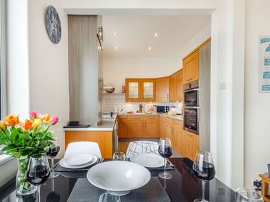 A kitchen with wooden cabinets a dining table with plates glasses and flowers at Little Orme View in Llandudno