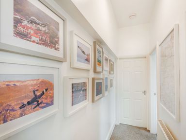 A hallway with framed pictures of airplanes on one wall and a door at the end at Little Orme View in Llandudno