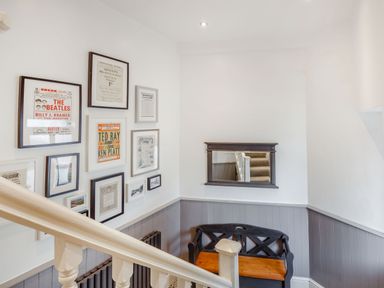 A stairwell with a black and wooden bench mirror on the wall and framed pictures at Little Orme View in Llandudno