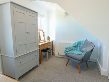 A bedroom with a wardrobe, chair, table and mirror at Little Orme View in Llandudno
