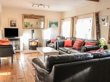 A living room with black leather sofas red cushions a white coffee table a fireplace and a television at Beulah Cottage in Green Bottom near Littledean
