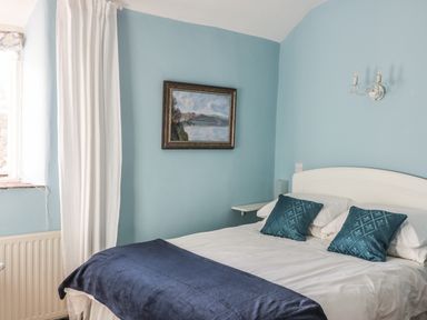 A bedroom with a white bed frame blue pillows blue blanket and a painting on the wall at Beulah Cottage in Green Bottom near Littledean