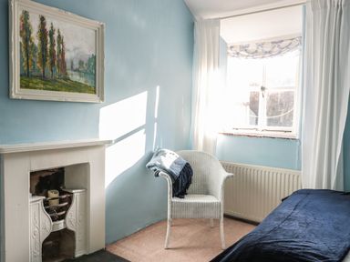 A room with a white chair with blankets near a window and a fireplace with a painting above at Beulah Cottage in Green Bottom near Littledean