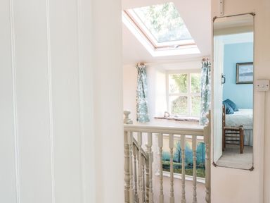 A staircase landing with a window curtain a skylight and a mirror reflecting a bedroom at Beulah Cottage in Green Bottom near Littledean