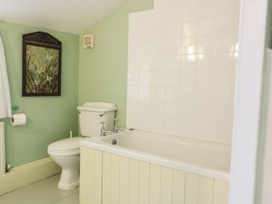 A bathroom with a toilet and bathtub with tiled wall and framed floral artwork at Beulah Cottage in Green Bottom near Littledean