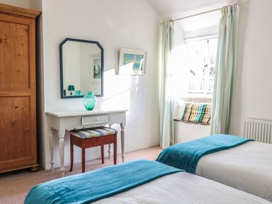 A bedroom with two beds blue blankets a wooden wardrobe a white dressing table a mirror and a window with curtains at Beulah Cottage Green Bottom near Littledean