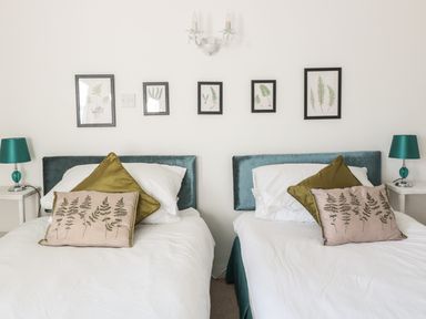 A bedroom with two single beds green headboards green and beige pillows framed botanical prints on the wall and matching side table lamps at Beulah Cottage in Green Bottom near Littledean