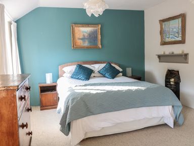A bedroom with a double bed two blue pillows wooden dressers paintings and a small fireplace at Beulah Cottage in Green Bottom near Littledean