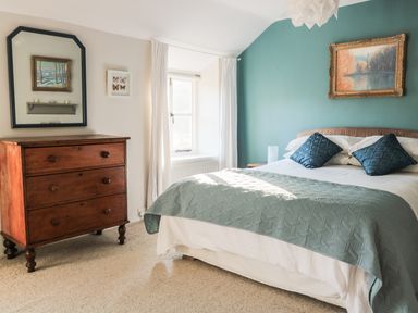 A bedroom with a bed with blue pillows a wooden chest of drawers a window and two paintings at Beulah Cottage Green Bottom near Littledean