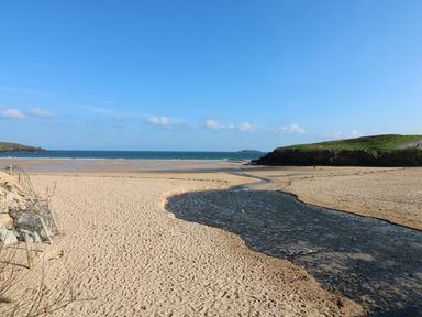 A beach with a stream flowing towards the sea and grassy hills in the background at Rockpool in Harlyn Bay near St Merryn