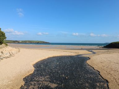 A sandy beach with a small stream flowing into the sea and grassy hills in the background at Rockpool in Harlyn Bay near St Merryn