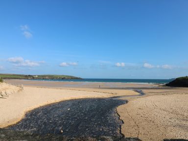 A beach with a river flowing into the sea and grassy hills in the background at Rockpool in Harlyn Bay near St Merryn