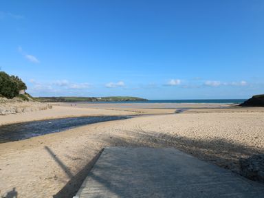 A sandy beach with a small stream running through it towards the sea at Rockpool in Harlyn Bay near St Merryn