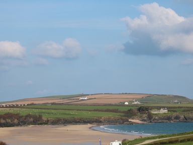 A beach with sand and ocean near green fields and houses at Rockpool in Harlyn Bay near St Merryn