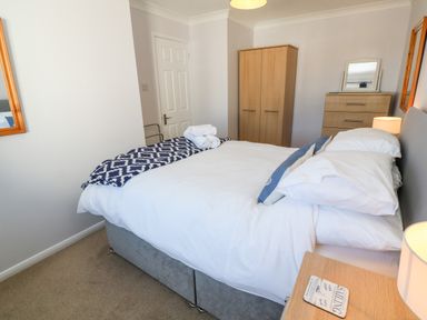 A bedroom with a double bed white bedding wooden wardrobe chest of drawers and bedside table at Rockpool in Harlyn Bay near St Merryn