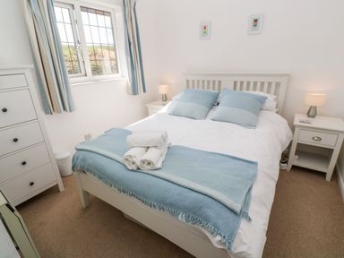 A bedroom with a bed with blue pillows and blanket towels on bed two nightstands with lamps and a chest of drawers at Rockpool in Harlyn Bay near St Merryn