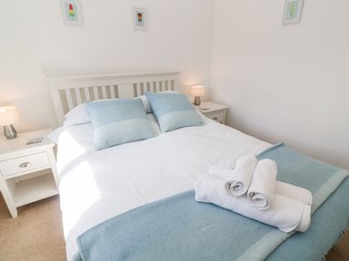 A bedroom with a white bed and blue pillows and blanket with rolled white towels on top at Rockpool in Harlyn Bay near St Merryn