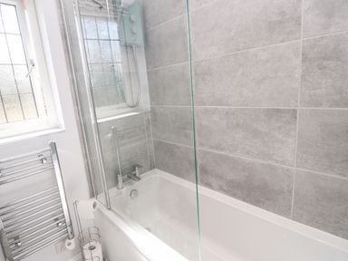 A bathroom with a bathtub shower and a towel rack at Rockpool in Harlyn Bay near St Merryn
