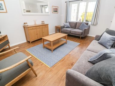 A living room with two gray sofas a wooden coffee table a cabinet and a window at Rockpool in Harlyn Bay near St Merryn