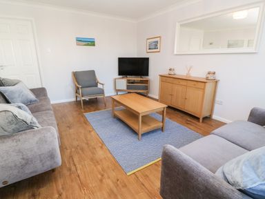 A living room with two sofas a wooden coffee table a wooden sideboard a TV on a stand and a blue patterned rug at Rockpool in Harlyn Bay near St Merryn