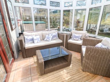 A sunroom with wicker furniture including two armchairs a sofa and a glass topped coffee table at Rockpool in Harlyn Bay near St Merryn