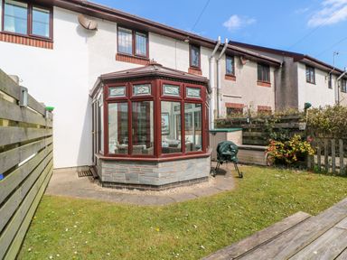 A backyard with grass a small patio a wooden fence and a conservatory at Rockpool in Harlyn Bay near St Merryn