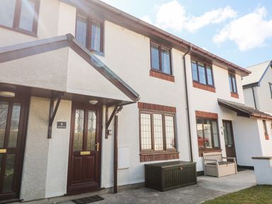 Exterior view of a white two story house with brown doors and windows with a covered porch and outdoor storage boxes at Rockpool in Harlyn Bay near St Merryn