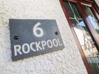 A black house number plaque with number 6 and text Rockpool on a rough white wall near a door with decorative glass panels at Rockpool in Harlyn Bay near St Merryn