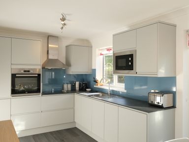 A kitchen with white cabinets a built in oven a microwave a toaster and a window at Rockpool in Harlyn Bay near St Merryn