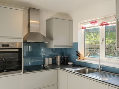 A kitchen with a sink under a window a stovetop with an oven a kettle a coffee machine and a knife block at Rockpool in Harlyn Bay near St Merryn
