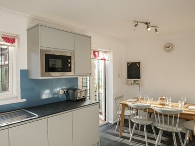 A kitchen with a microwave, toaster, dining table with chairs and glassware at Rockpool in Harlyn Bay near St Merryn