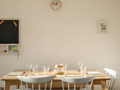 A dining table set with glasses and cutlery in a room with a clock and framed picture on the wall at Rockpool in Harlyn Bay near St Merryn