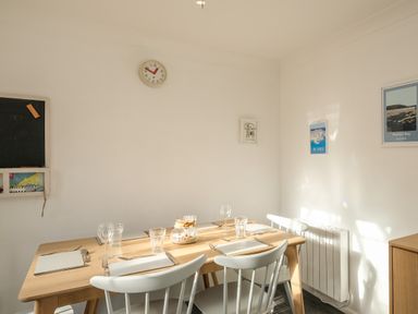 A dining room with a wooden table set for four with plates glasses and cutlery and four white chairs at Rockpool in Harlyn Bay near St Merryn